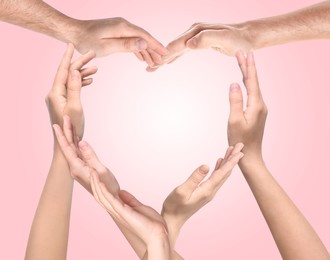 Image of People making heart shape with hands on pink background. Teamwork, unity, togetherness