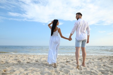 Photo of Happy young couple walking together on beach, back view