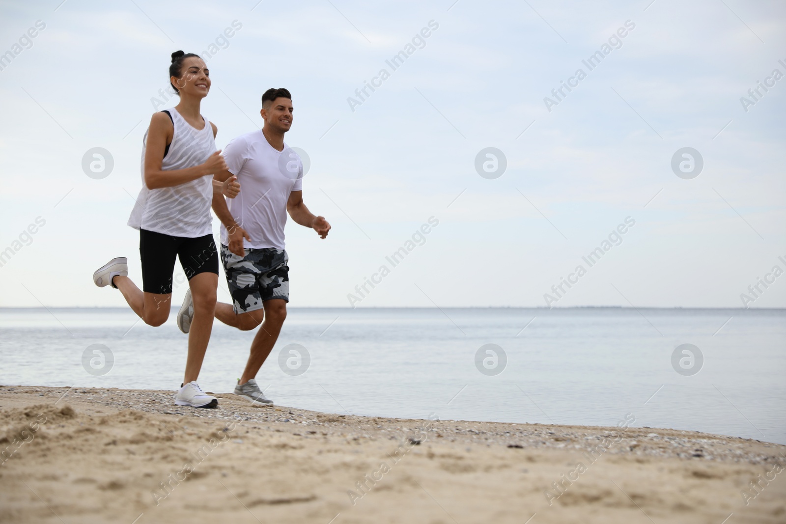 Photo of Couple running together on beach, space for text. Body training