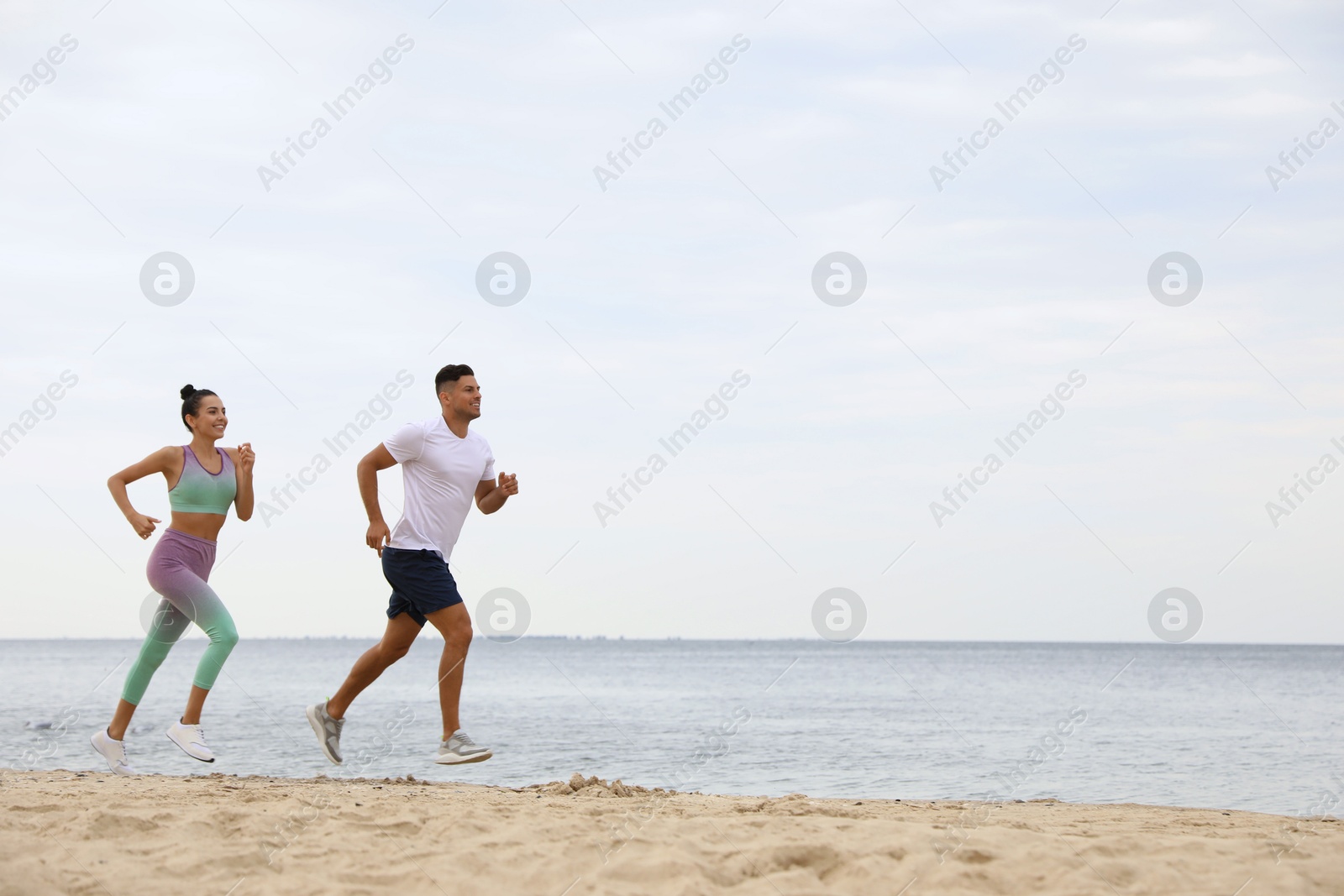 Photo of Couple running together on beach, space for text. Body training