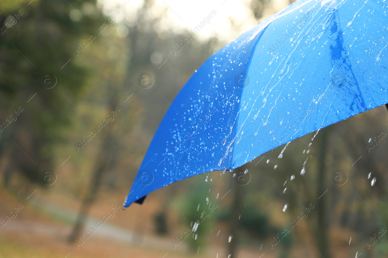 Photo of Open blue umbrella under pouring rain outdoors, closeup. Space for text