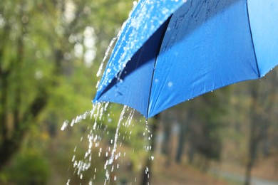 Photo of Open blue umbrella under pouring rain outdoors, closeup