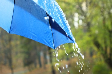 Photo of Open blue umbrella under pouring rain outdoors, closeup