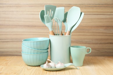 Photo of Dishware, cooking utensils and garlic on wooden table