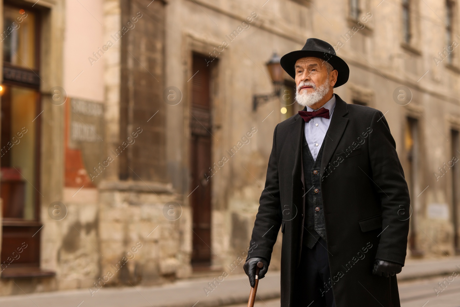 Photo of Elegant senior man with walking cane on city street. Space for text