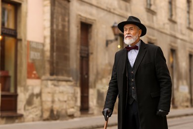 Photo of Elegant senior man with walking cane on city street. Space for text