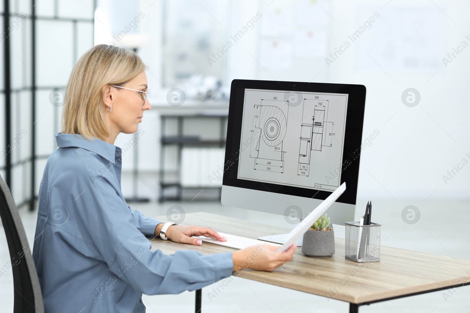 Photo of Technician making digital engineering drawing on computer at desk in office