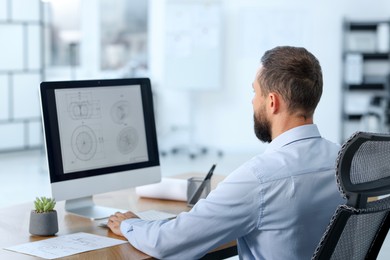 Photo of Technician making digital engineering drawing on computer at desk in office, back view