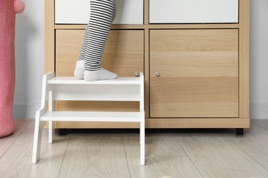 Photo of Little girl standing on step stool indoors, closeup