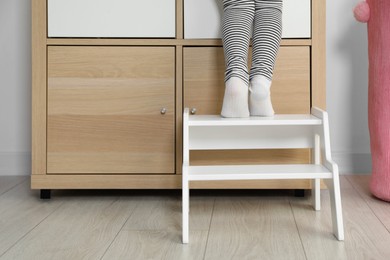 Photo of Little girl standing on step stool indoors, closeup