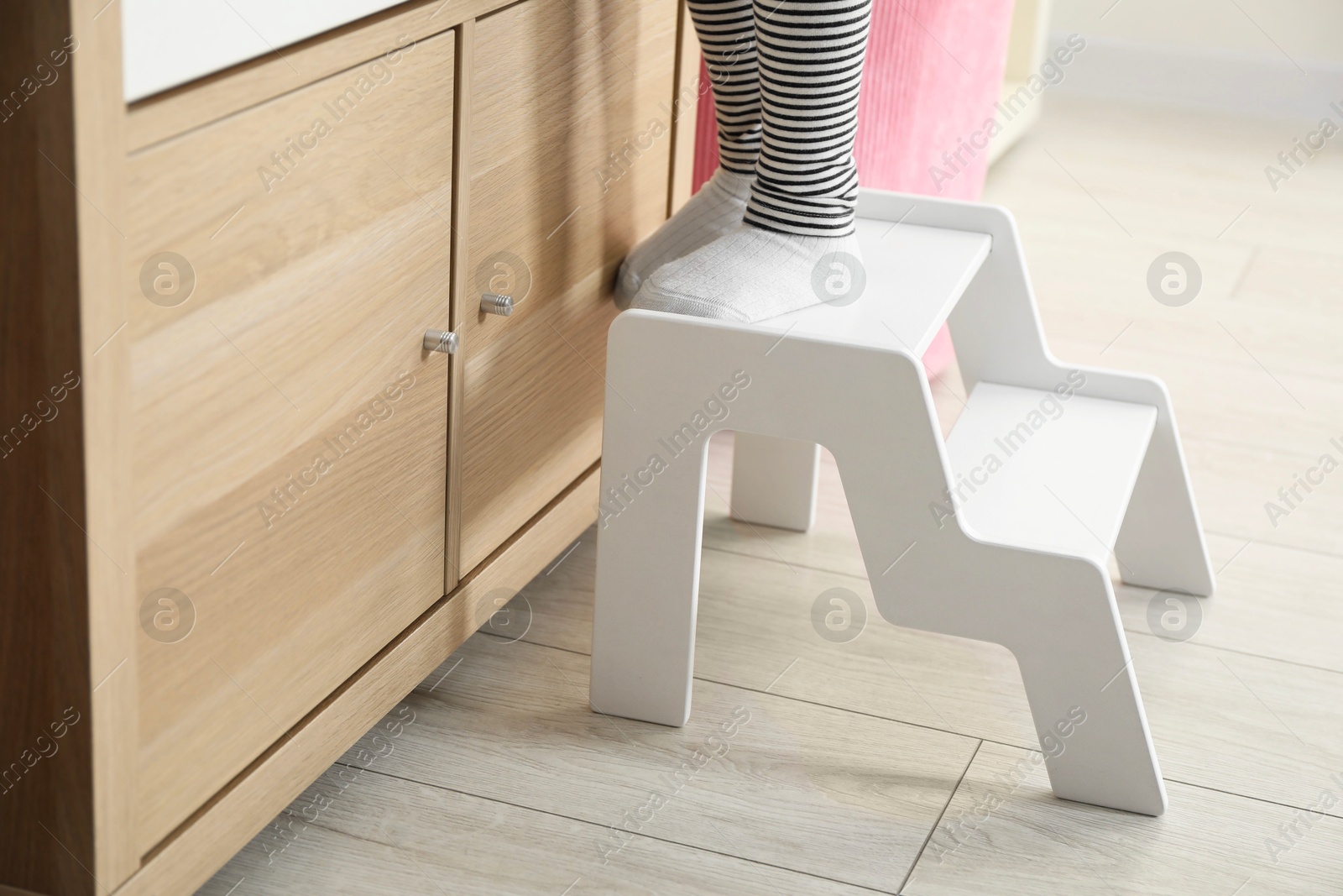 Photo of Little girl standing on step stool indoors, closeup