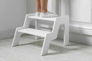 Photo of Little girl standing on step stool indoors, closeup