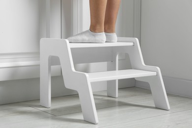 Photo of Little girl standing on step stool indoors, closeup