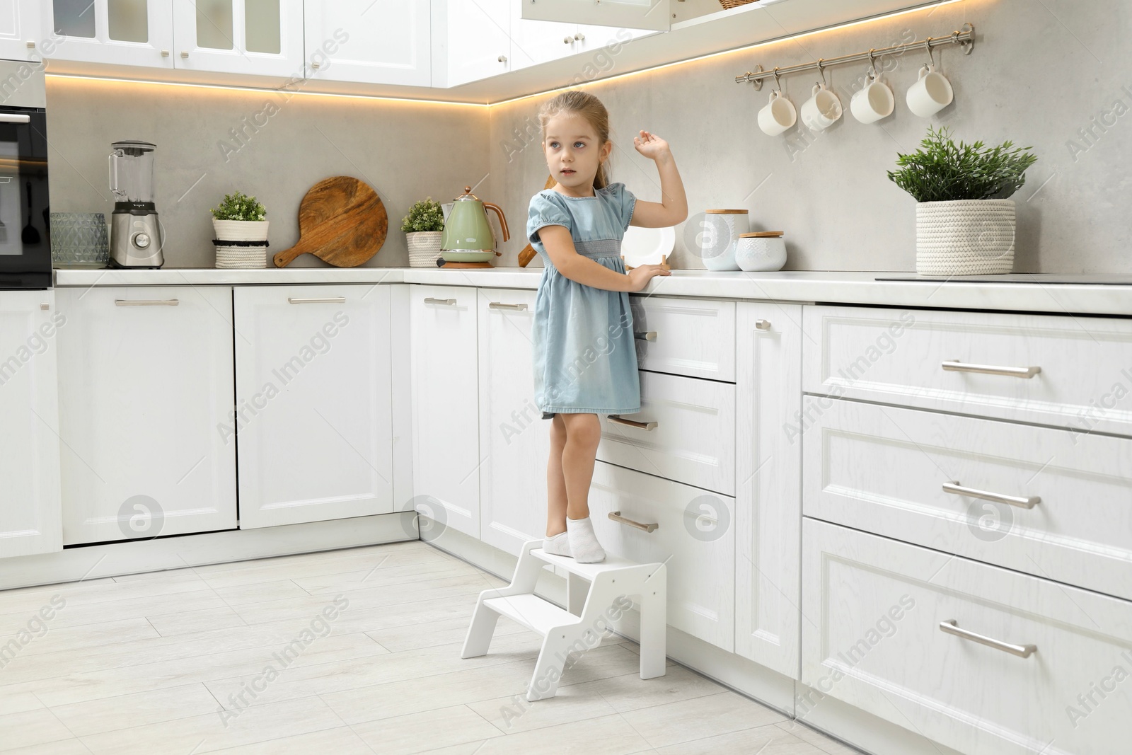 Photo of Little girl standing on step stool and reaching towards counter in kitchen