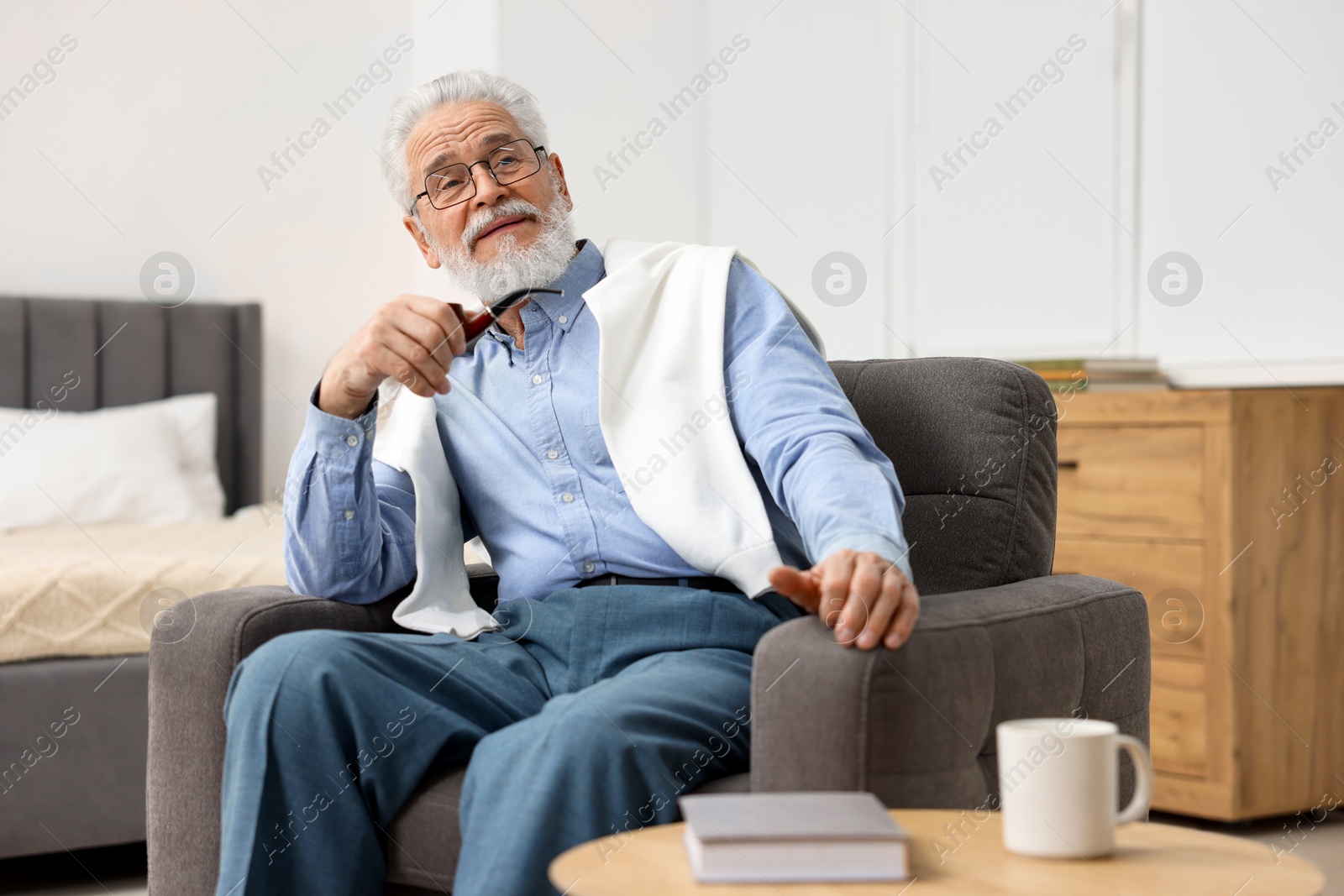 Photo of Handsome bearded man with tobacco pipe in armchair indoors