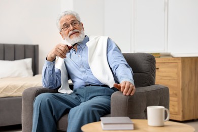 Photo of Handsome bearded man with tobacco pipe in armchair indoors