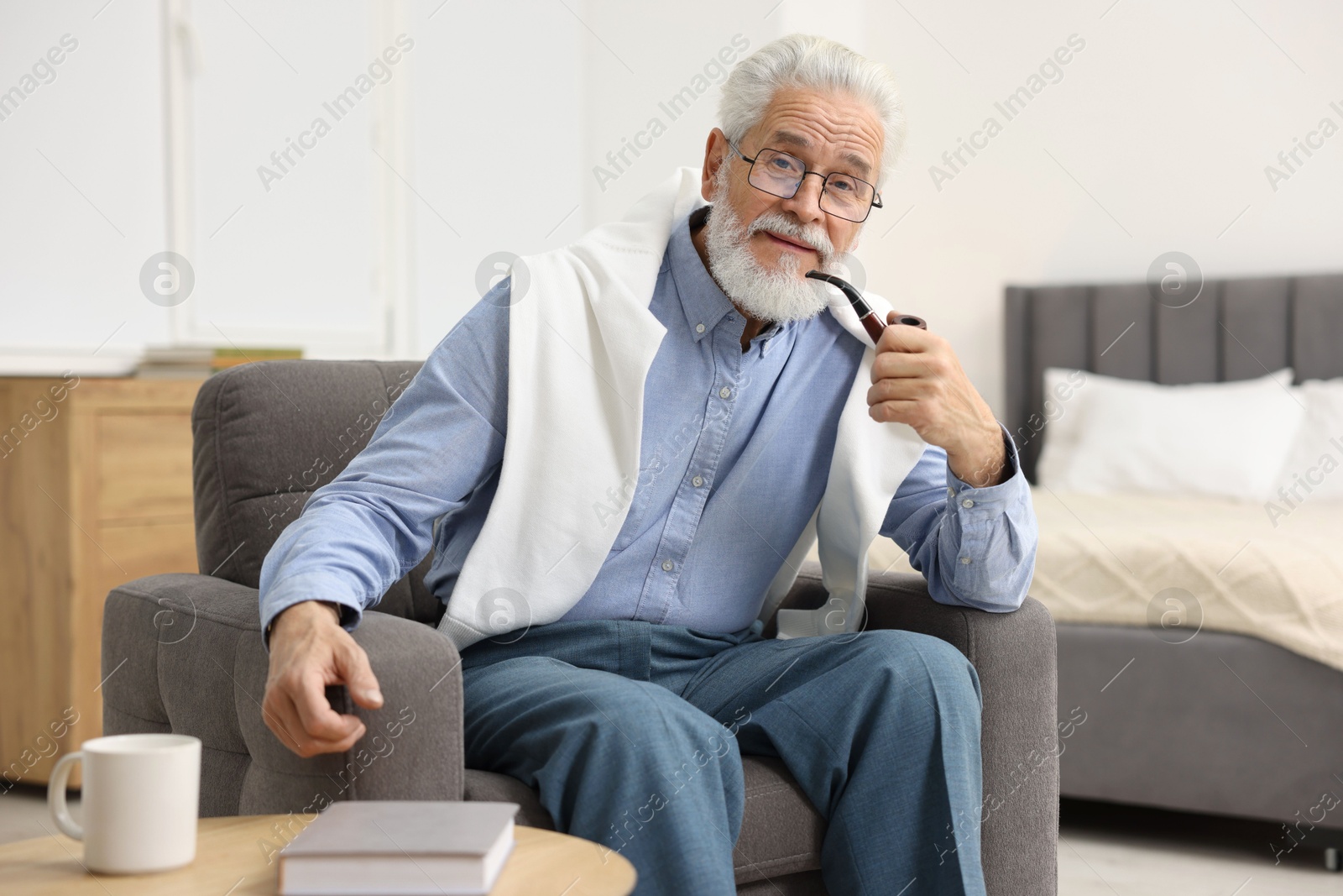 Photo of Handsome bearded man with tobacco pipe in armchair indoors