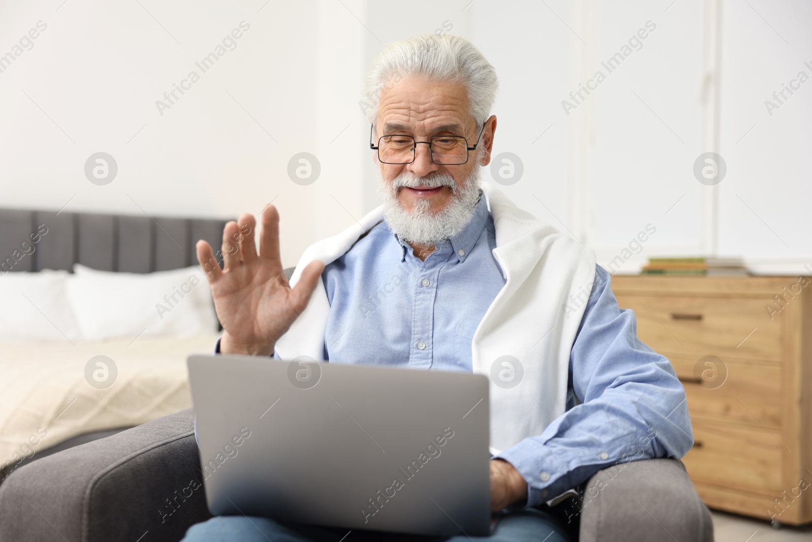 Photo of Bearded man having video chat via laptop in armchair indoors