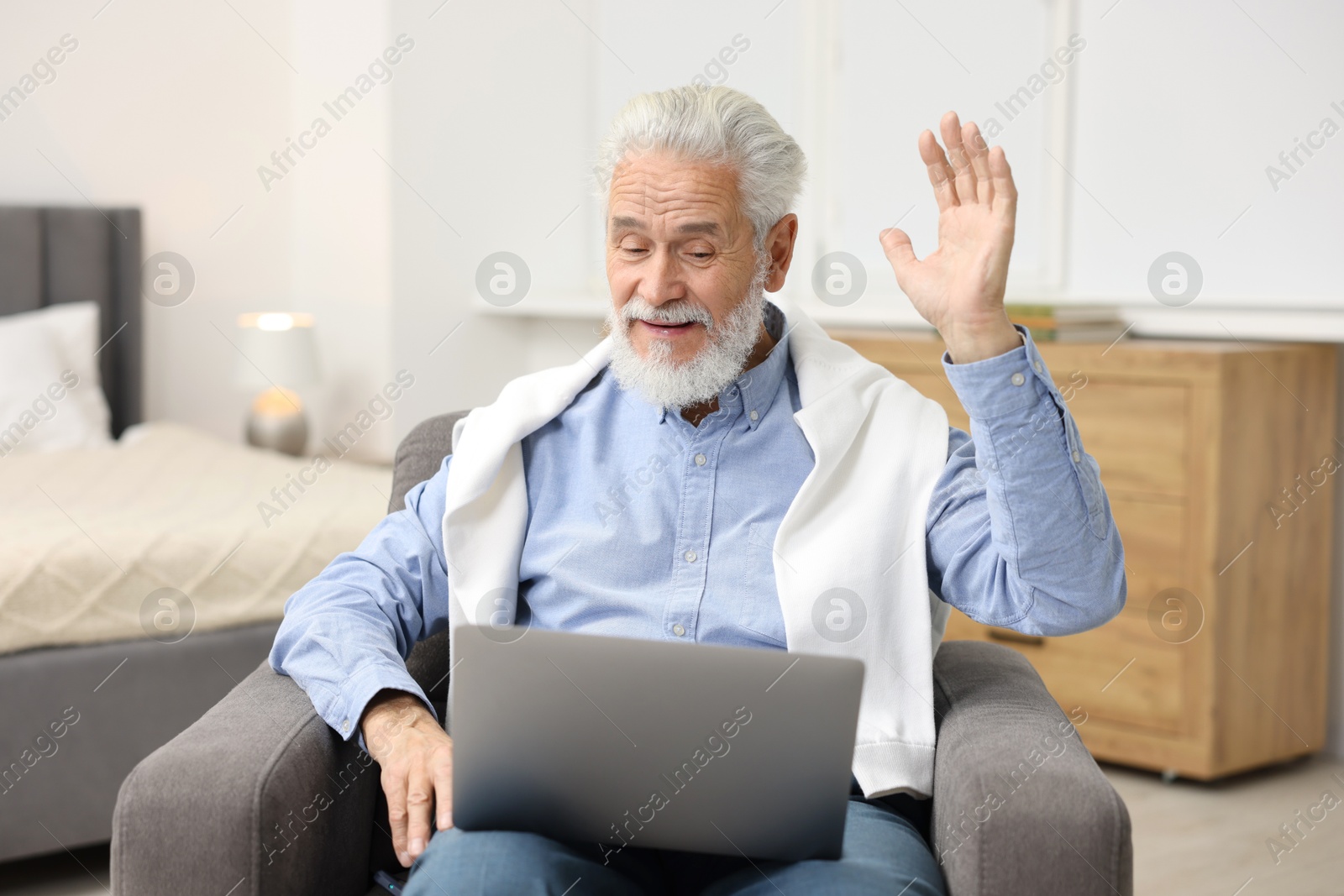 Photo of Bearded man having video chat via laptop in armchair indoors