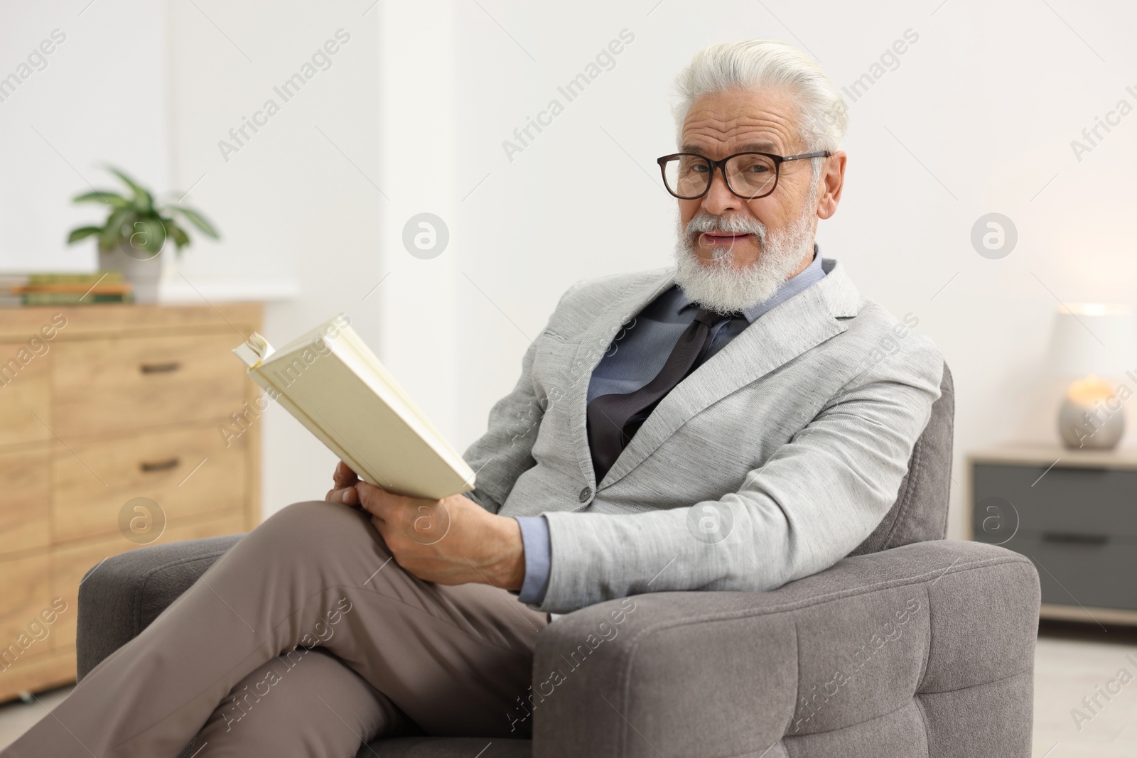 Photo of Handsome bearded man reading book in armchair indoors