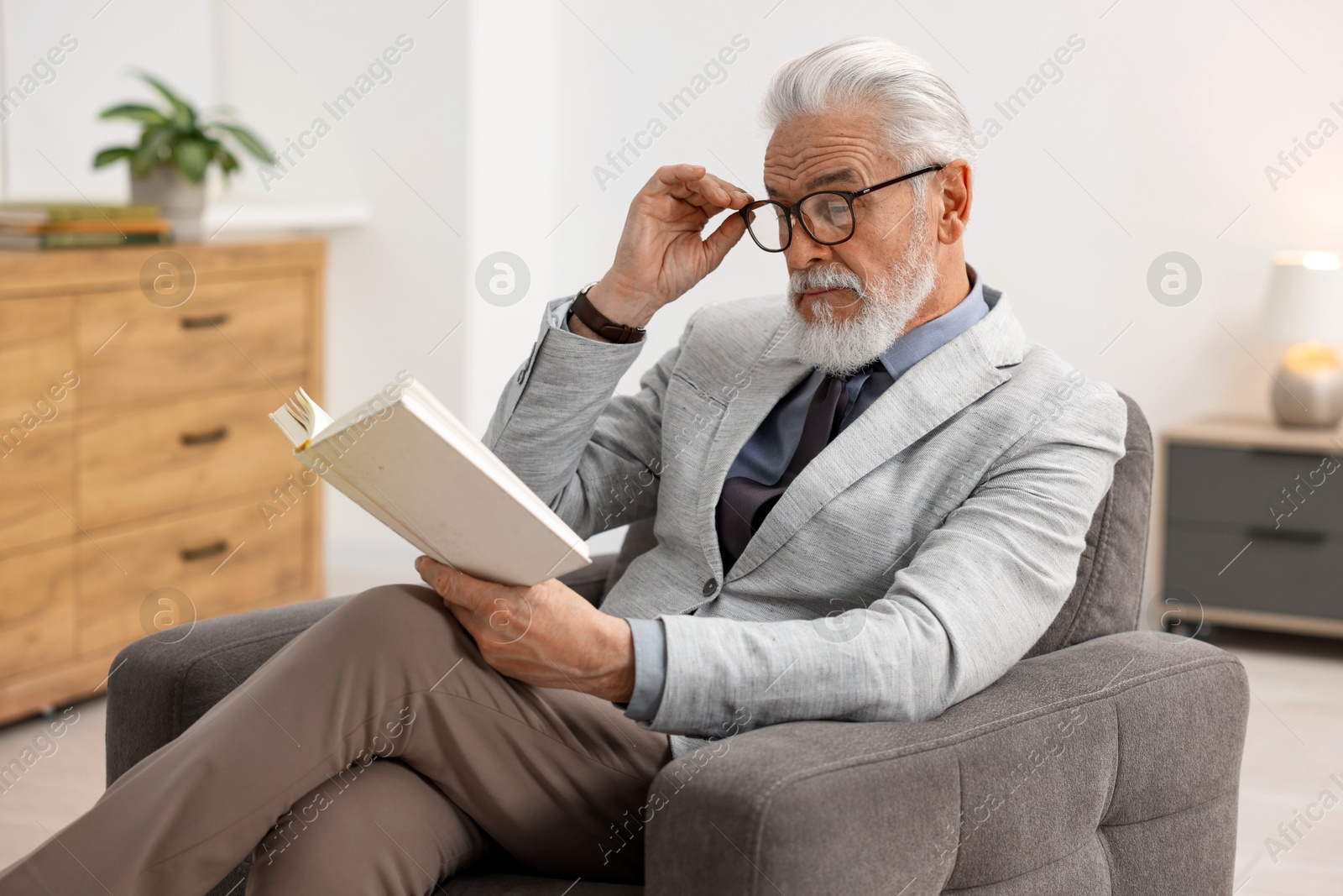 Photo of Handsome bearded man reading book in armchair indoors