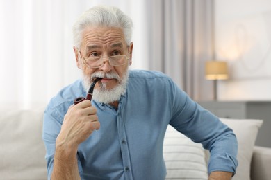 Photo of Handsome bearded man with tobacco pipe on sofa indoors