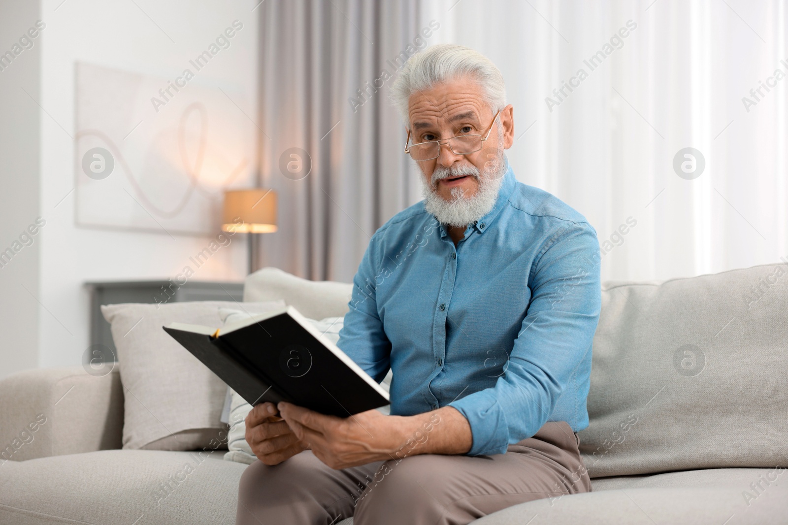 Photo of Handsome bearded man with book on sofa indoors