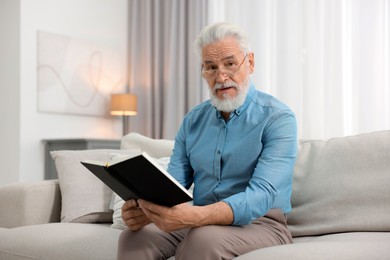 Photo of Handsome bearded man with book on sofa indoors