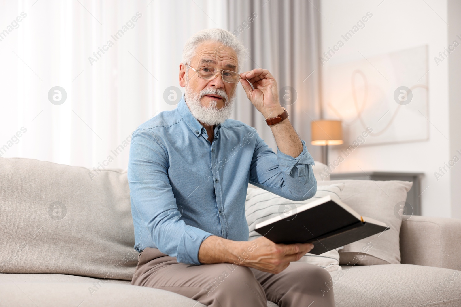 Photo of Handsome bearded man with book on sofa indoors