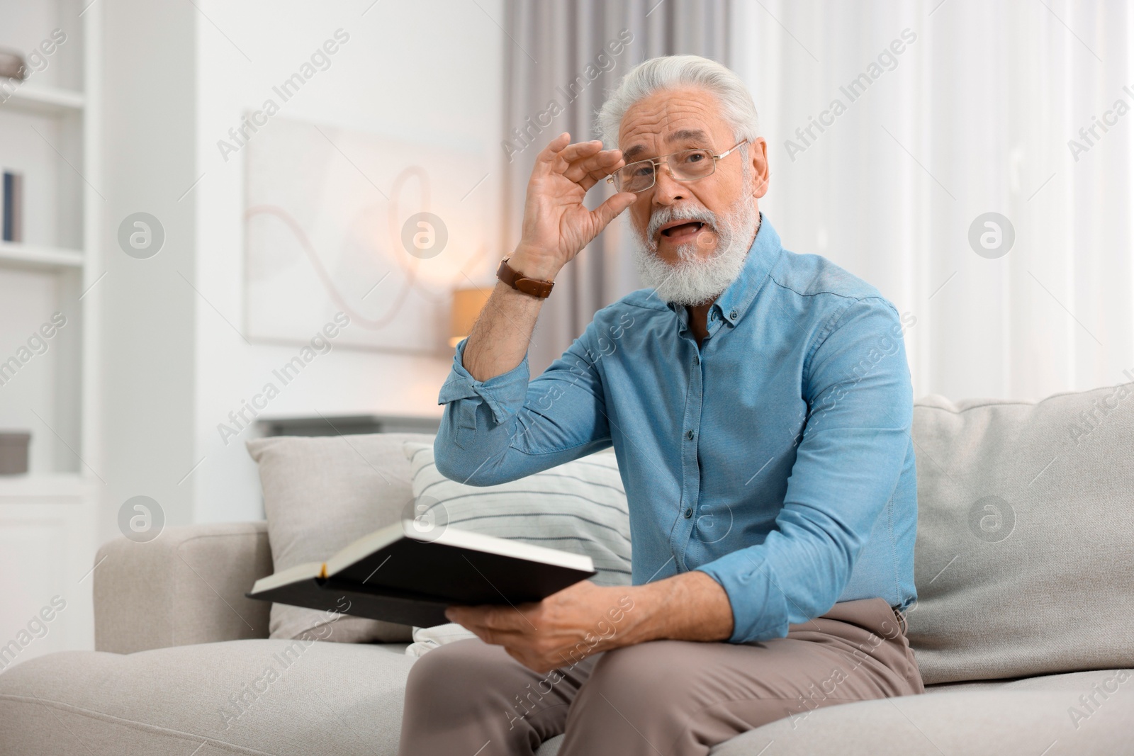 Photo of Handsome bearded man with book on sofa indoors