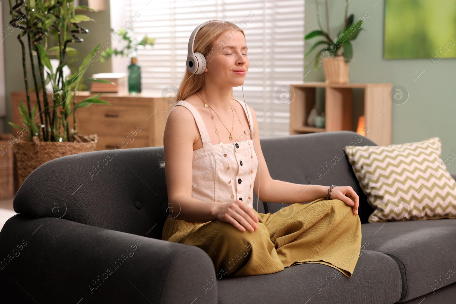 Photo of Feng shui. Young woman with headphones meditating on couch at home''