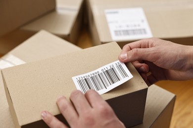 Photo of Man sticking barcode on parcel indoors, closeup