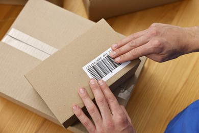 Photo of Man sticking barcode on parcel at wooden table indoors, above view