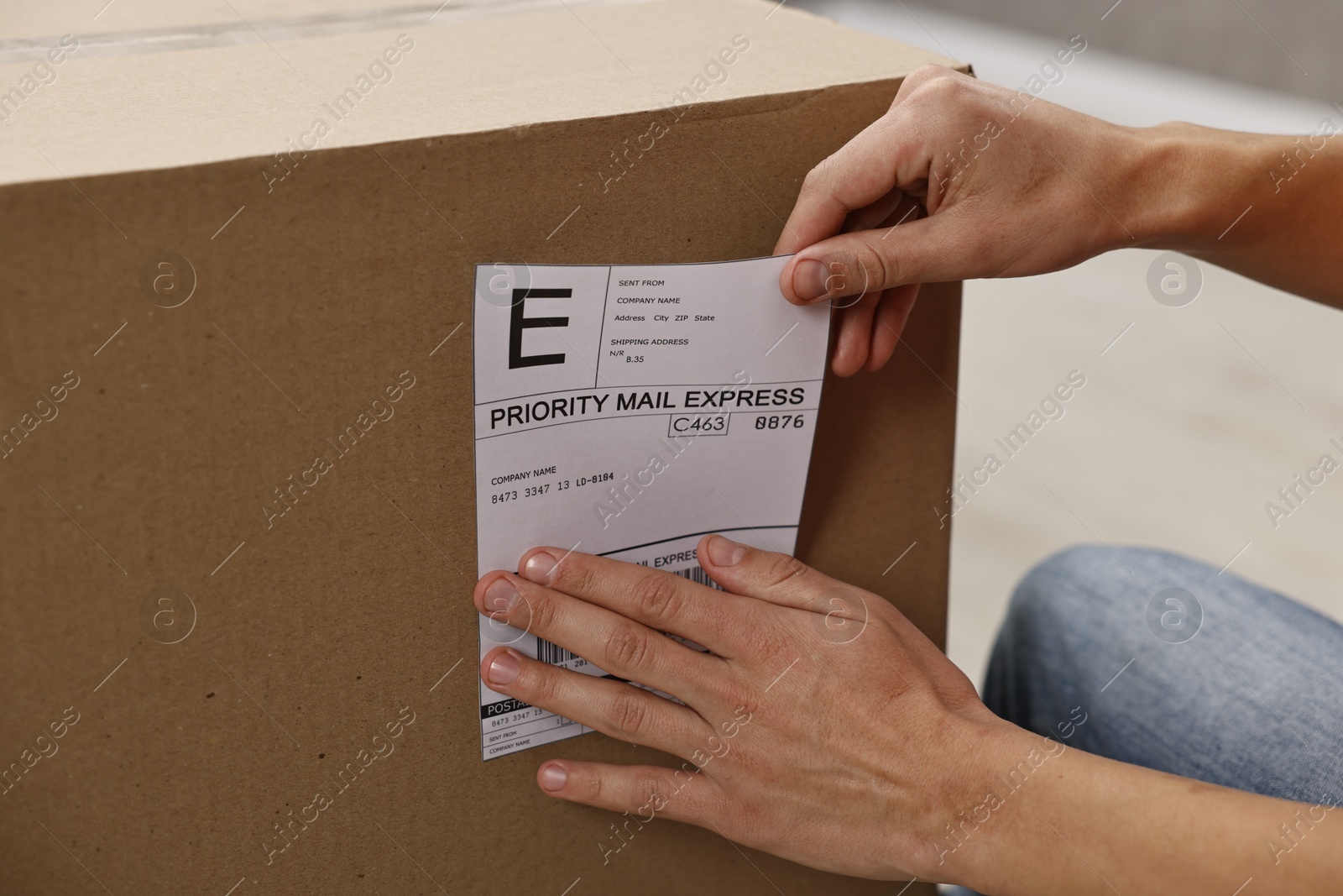 Photo of Man sticking shipping label with barcode on parcel indoors, closeup