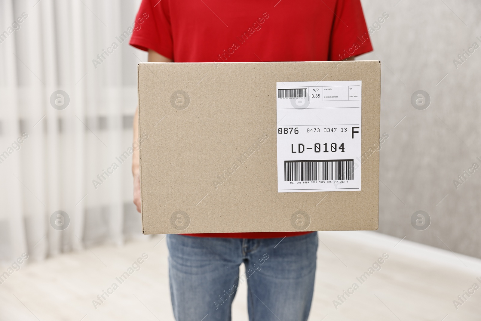 Photo of Man holding parcel with shipping label indoors, closeup