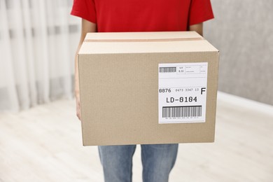 Photo of Man holding parcel with shipping label indoors, closeup