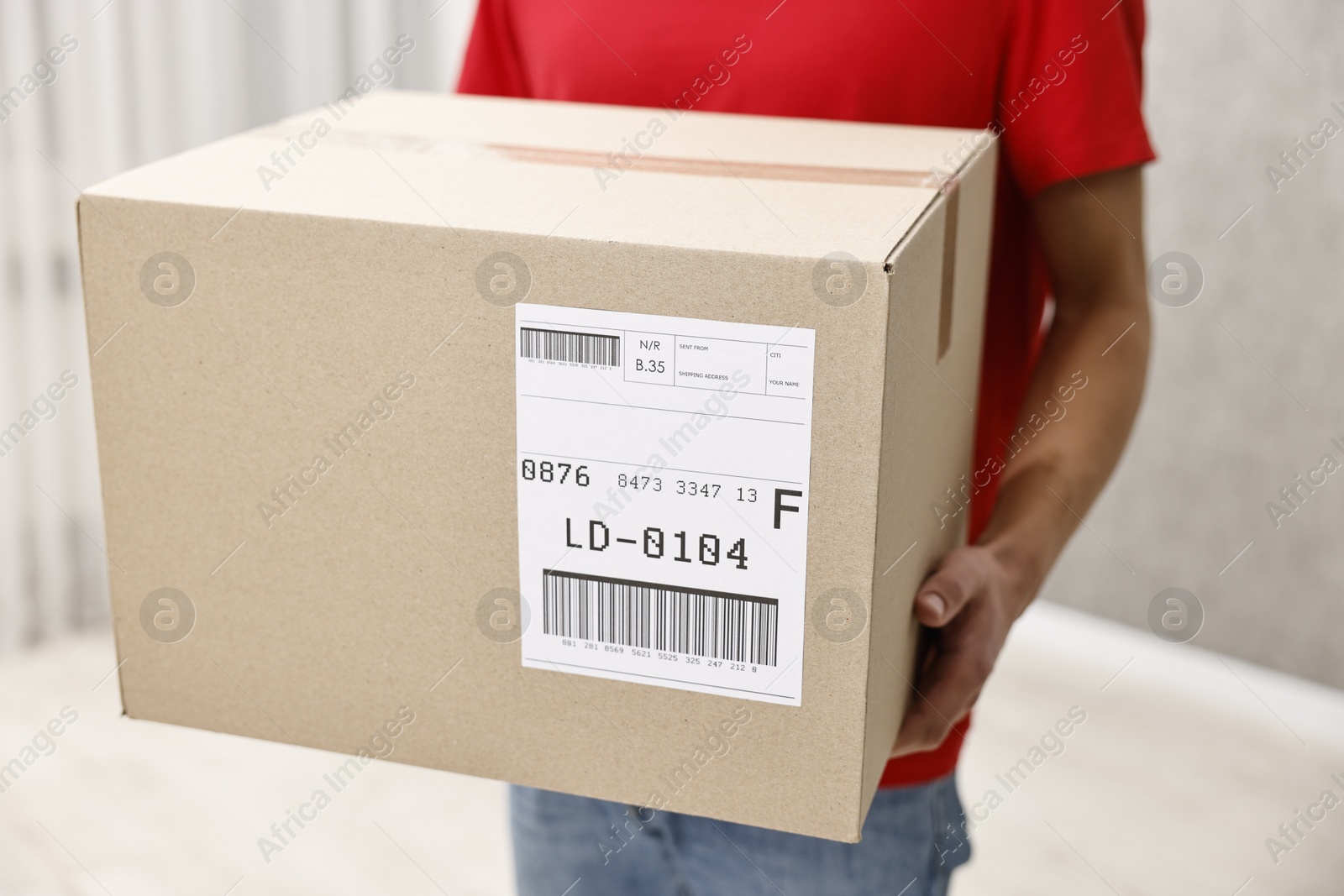 Photo of Man holding parcel with shipping label indoors, closeup