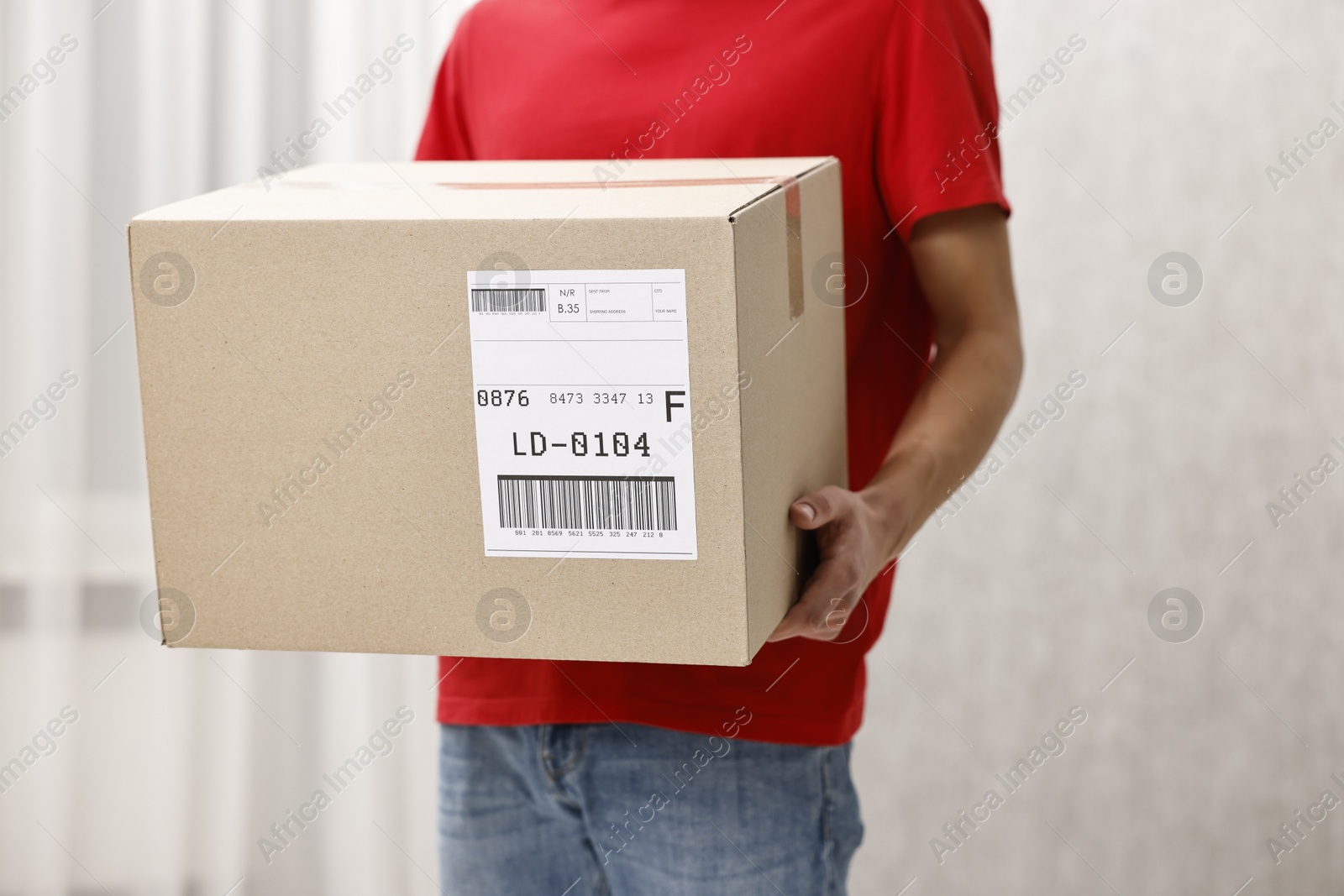 Photo of Man holding parcel with shipping label indoors, closeup. Space for text