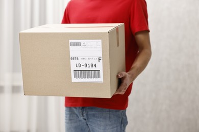 Photo of Man holding parcel with shipping label indoors, closeup. Space for text