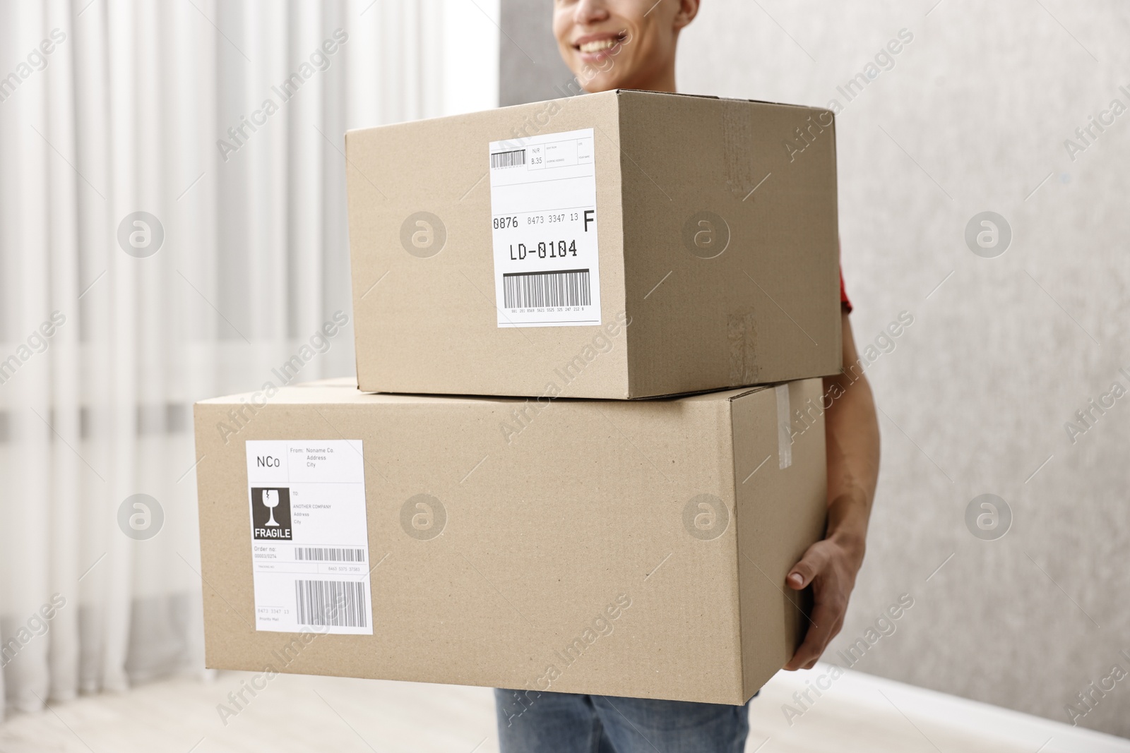 Photo of Man holding parcels with shipping labels indoors, closeup