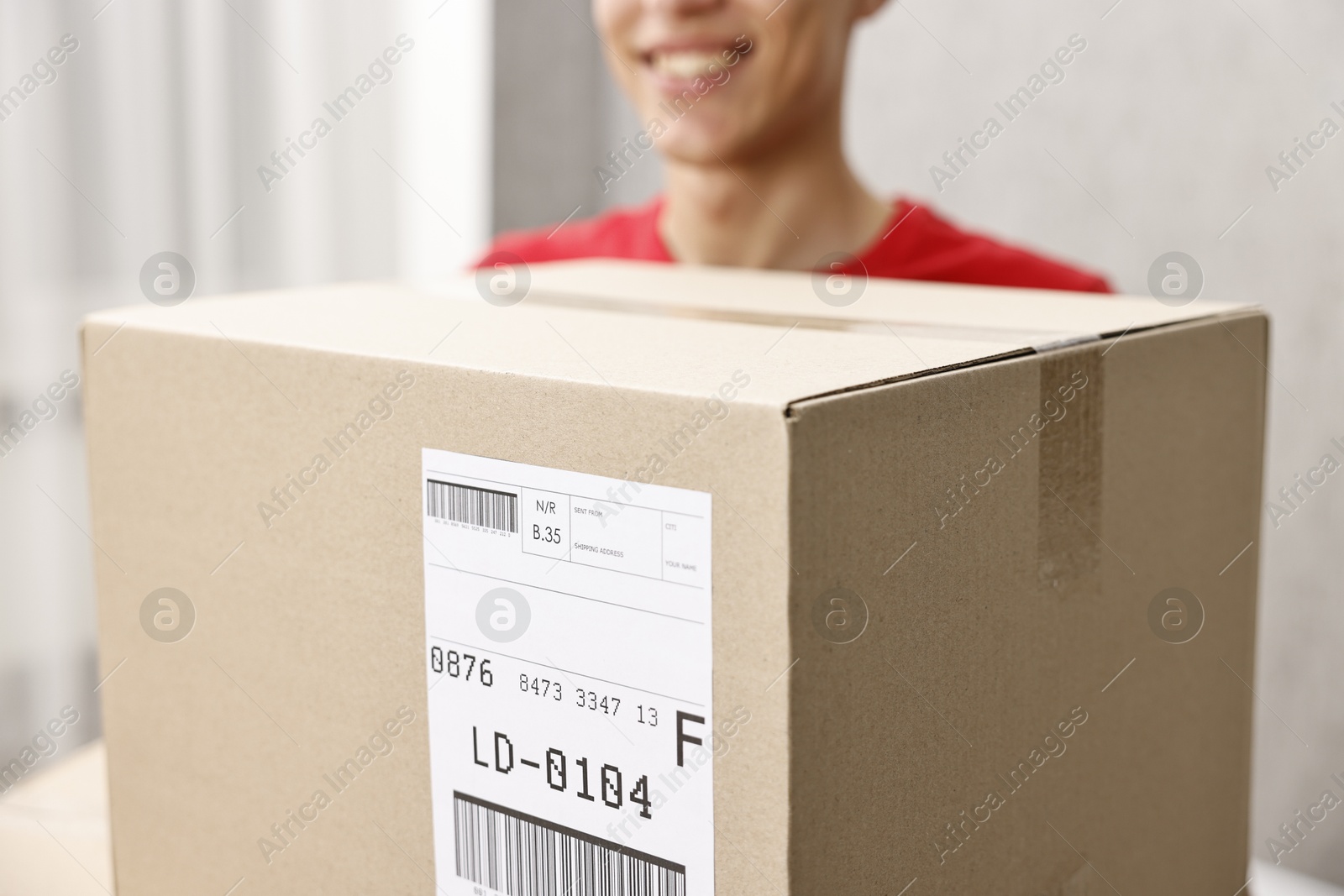 Photo of Man holding parcel with shipping label indoors, closeup