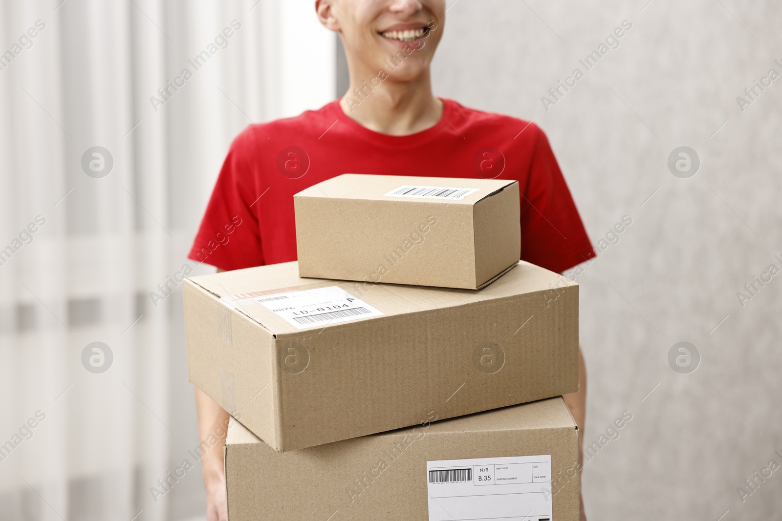 Photo of Man holding parcels with shipping labels indoors, closeup