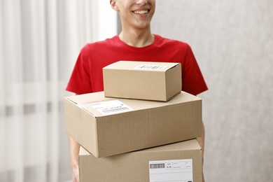 Photo of Man holding parcels with shipping labels indoors, closeup