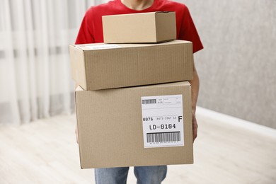 Photo of Man holding parcels with shipping labels indoors, closeup