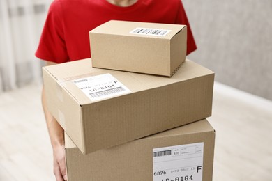 Photo of Man holding parcels with shipping labels indoors, closeup