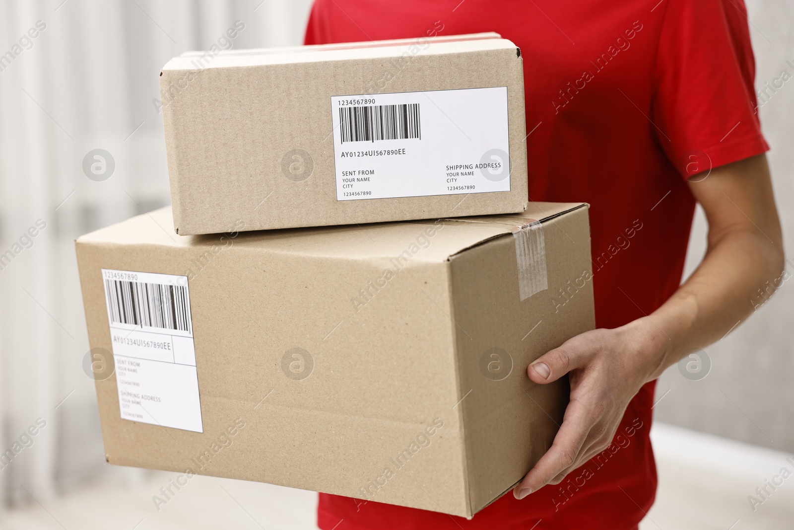 Photo of Man holding parcels with shipping labels indoors, closeup