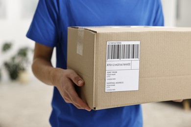 Man holding parcel with shipping label indoors, closeup