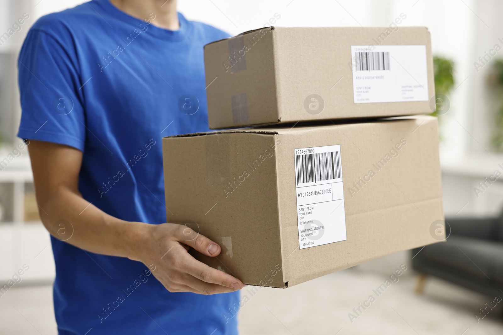 Photo of Man holding parcels with shipping labels indoors, closeup