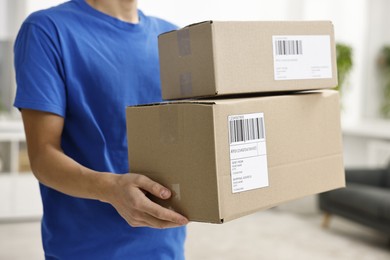 Man holding parcels with shipping labels indoors, closeup