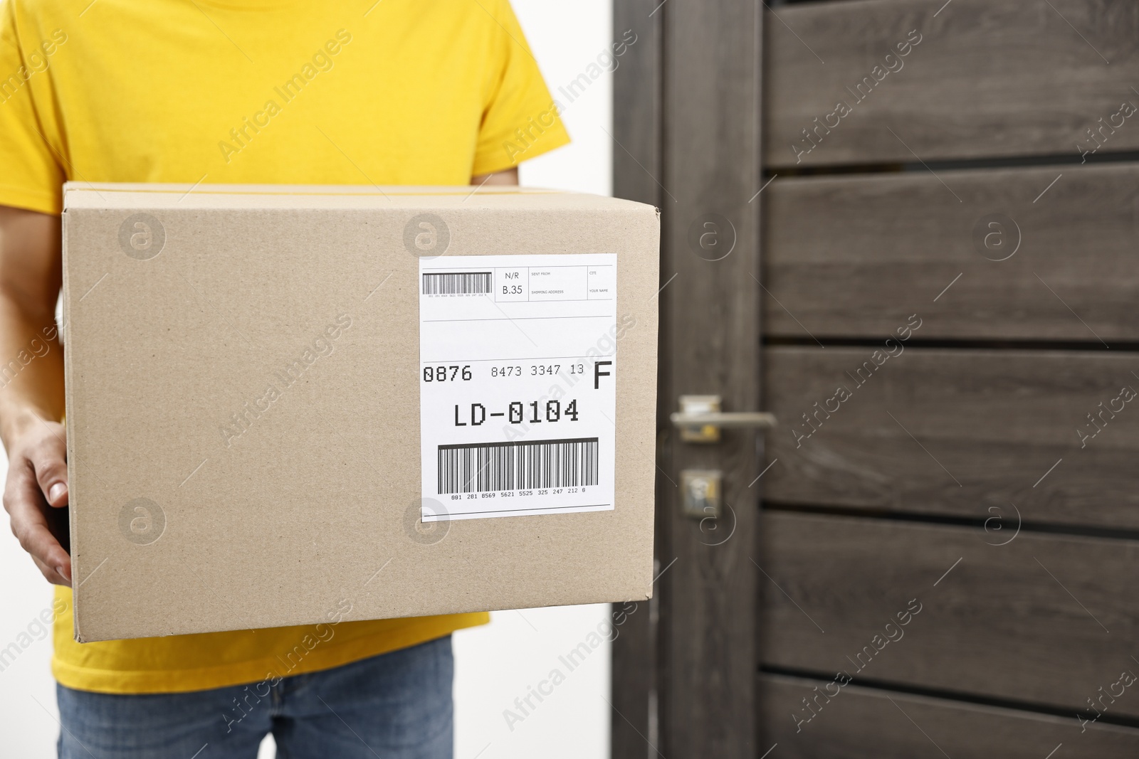 Photo of Man holding parcel with shipping label near door indoors, closeup. Space for text